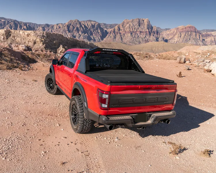 A red Ford F-150 Raptor with a folding bed cover in the desert